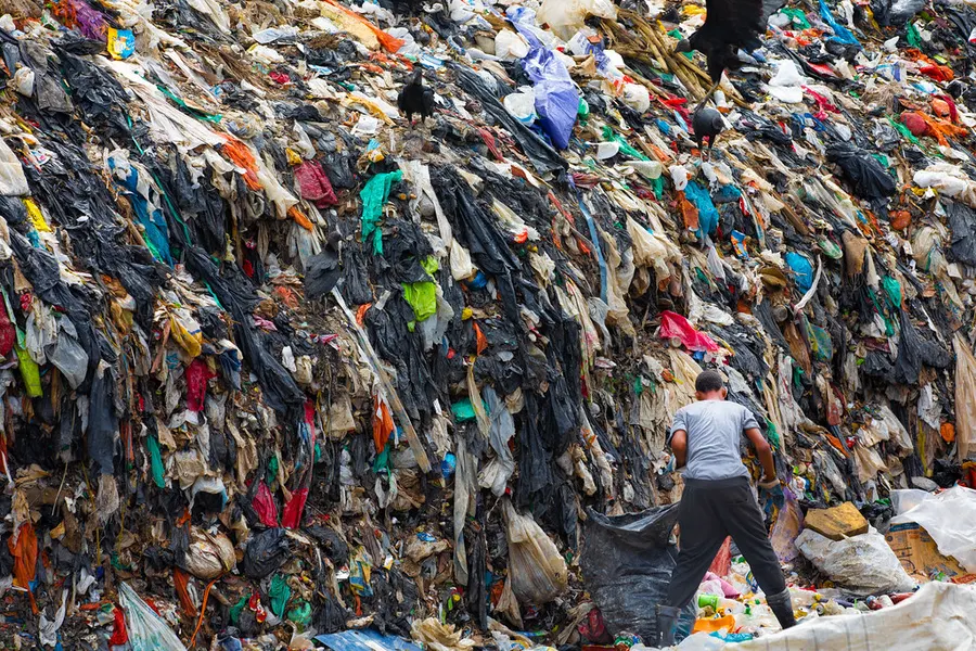 Worker beside a towering landfill heap of mixed waste